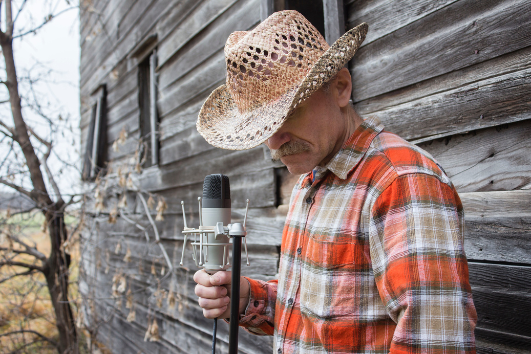 country singer wearing cowboy hat standing against old wooden wall